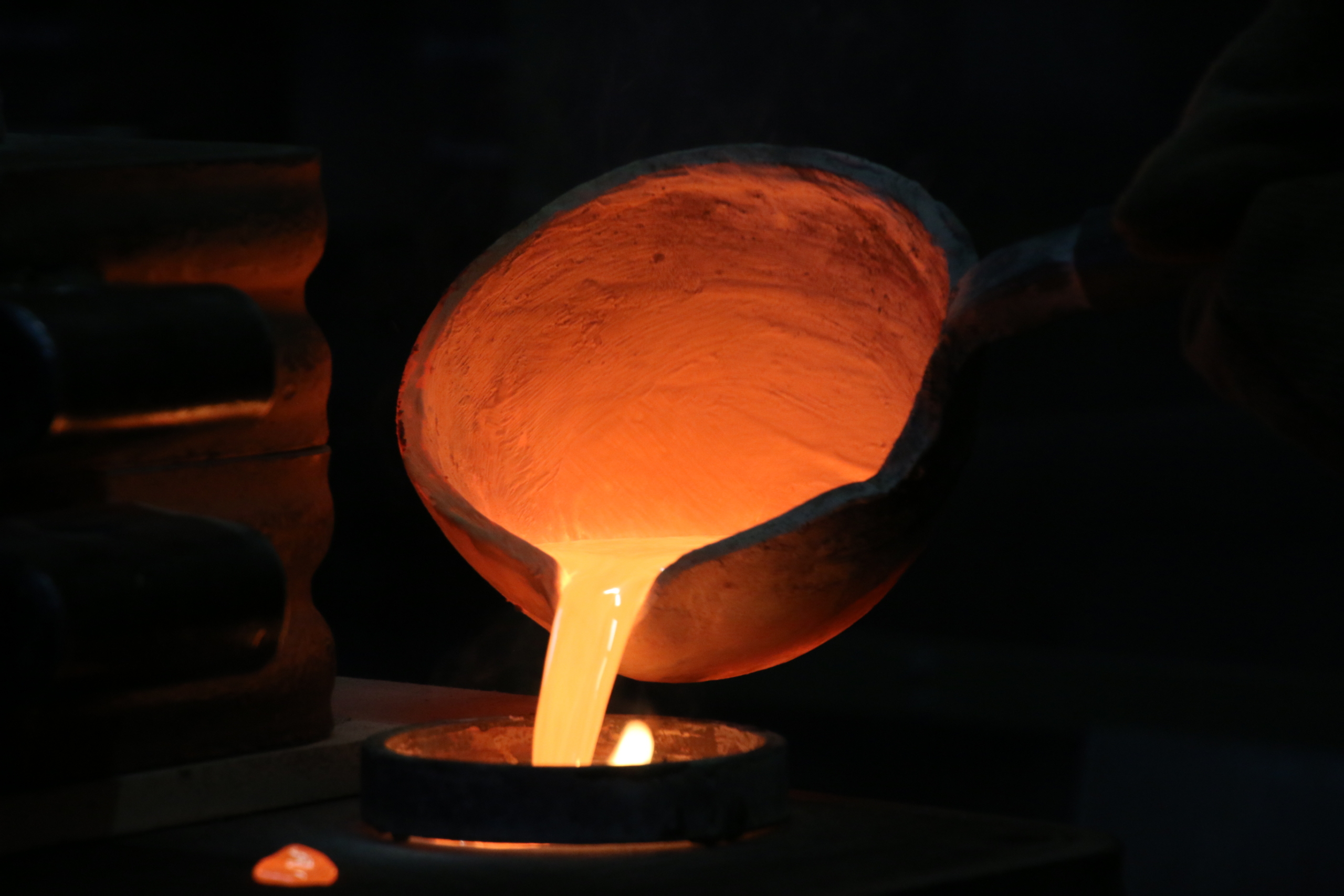 Flüssige Bronze fliesst aus der glühenden Gusskelle in eine Sandform